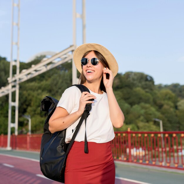 Mulher sorridente viajando com mochila usando fones de ouvido