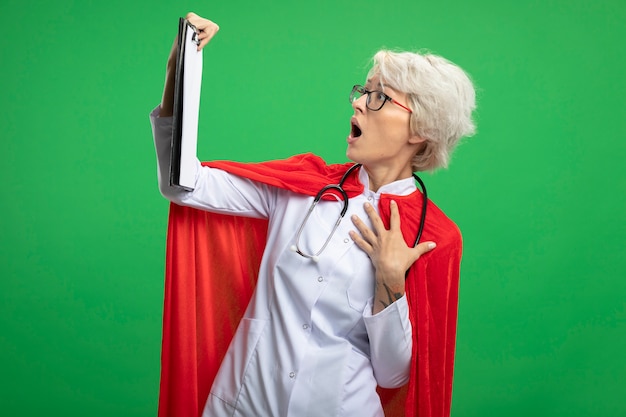 Foto grátis mulher super-heroína eslava chocada em uniforme de médico com capa vermelha e estetoscópio em óculos ópticos