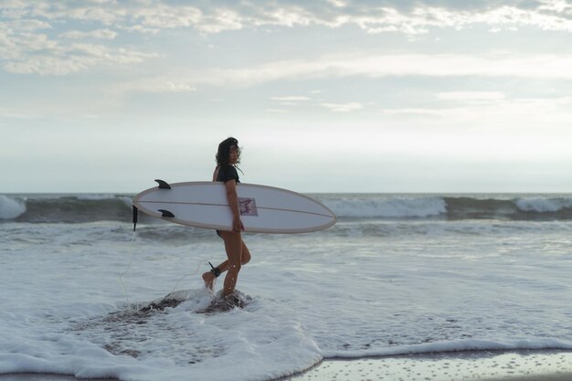 Mulher surfista com prancha de surf no oceano ao pôr do sol