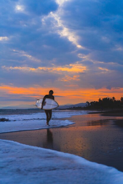Mulher surfista com prancha de surf no oceano ao pôr do sol.