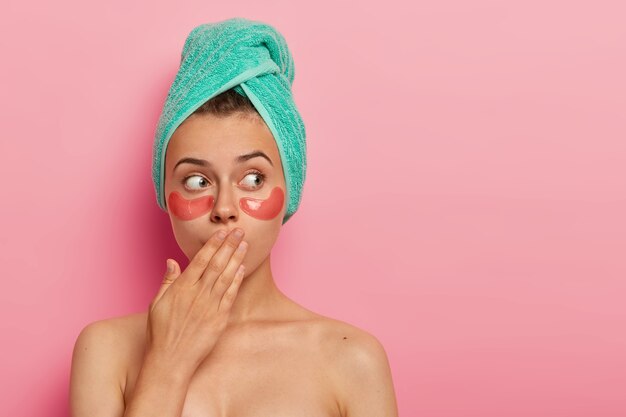 Mulher surpreendida cobre a boca, usa adesivos cosméticos sob os olhos. Tratamento facial e conceito de beleza