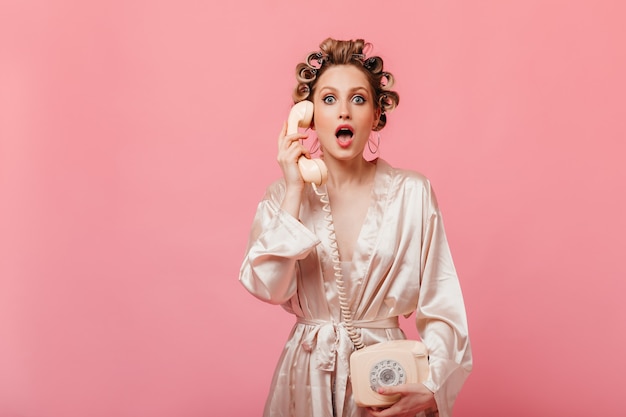 Foto grátis mulher surpreendida em roupão de banho, olhando para a frente e segurando um telefone fixo na parede isolada