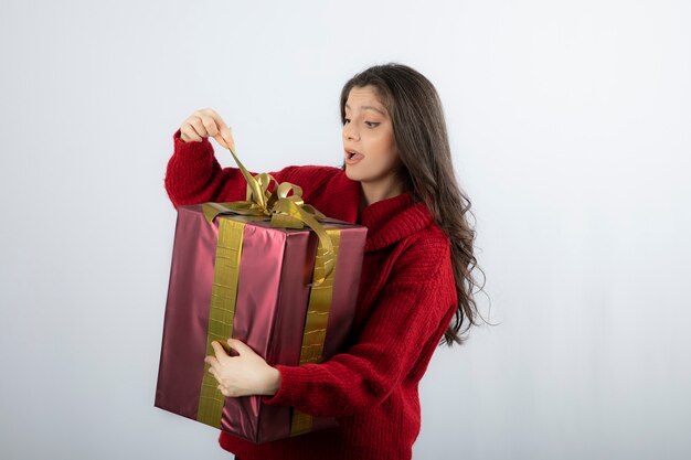 Mulher surpreendida num suéter vermelho, abrindo uma caixa de presente de Natal.