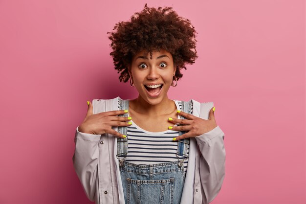 Foto grátis mulher surpresa, animada e cheia de alegria parece feliz, mantém as mãos no peito, feliz por receber a surpresa, usa roupas casuais e anoraque, faz manicure brilhante, abre a boca amplamente enquanto ri