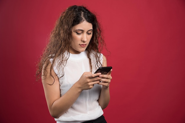 Mulher surpresa digitando algo em seu celular no vermelho