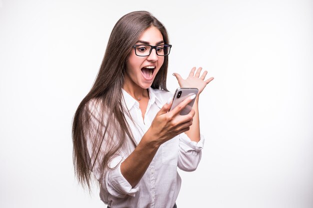 Mulher surpresa muito feliz posando com o celular na parede branca