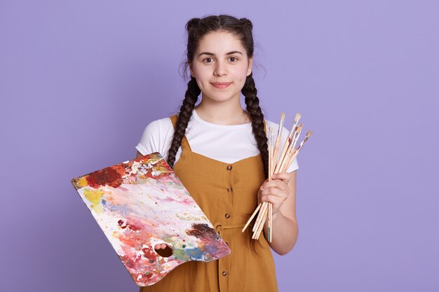 Mulher talentosa, criando um lindo desenho floral em aquarela, isolado sobre uma parede lilás, vestindo roupas casuais.