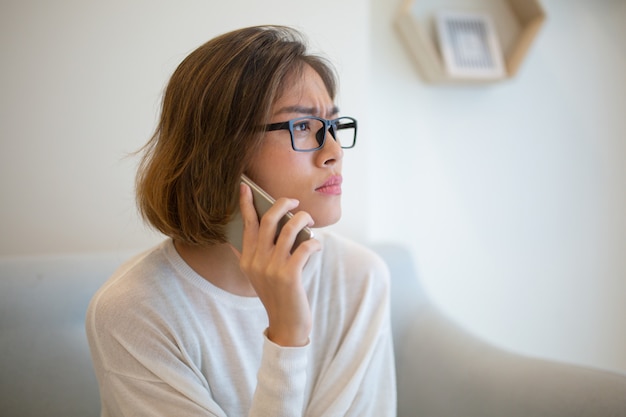 Mulher tensa chamando no smartphone no sofá em casa