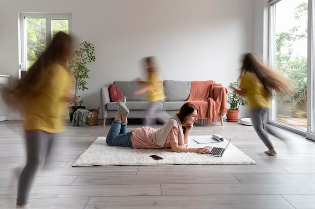 Mulher tentando trabalhar em um laptop de casa enquanto os filhos estão correndo