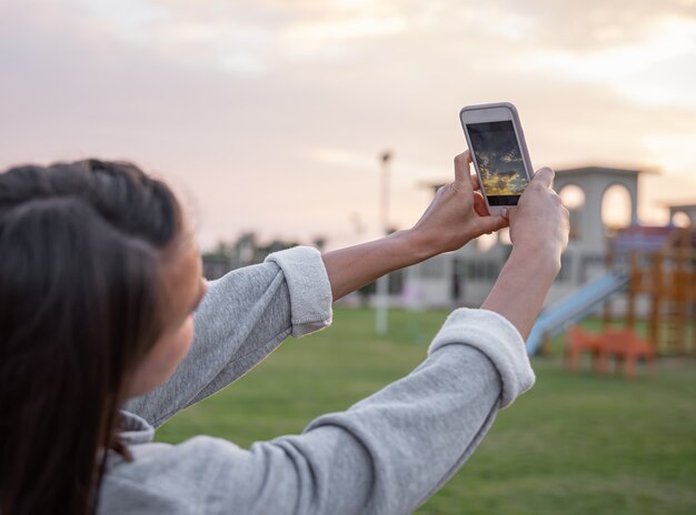 Mulher tira uma foto do céu ao pôr do sol em seu celular.