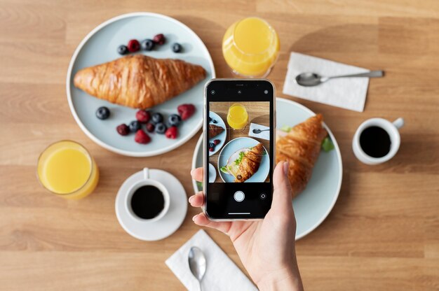 Mulher tirando foto de um croissant e um copo de suco de laranja