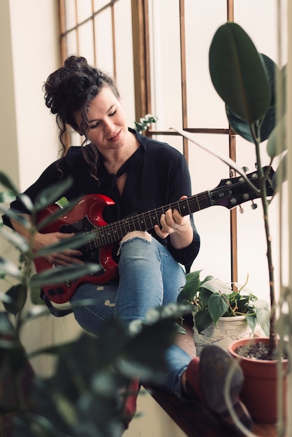 Mulher tocando na guitarra ao lado de plantas