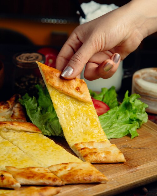 Mulher tomando uma fatia de pão turco pide com queijo derretido.