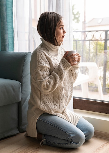 Foto grátis mulher tomando uma xícara de café ao lado da janela em casa durante a pandemia