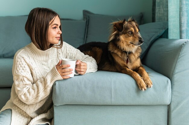 Mulher tomando uma xícara de café ao lado de seu cachorro em casa durante a pandemia
