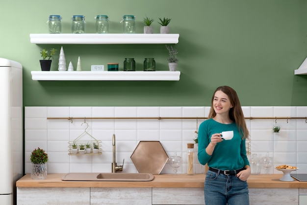 Foto grátis mulher tomando uma xícara de café em uma cozinha verde