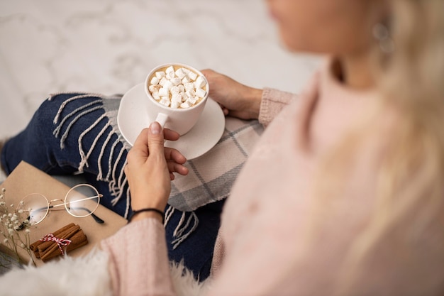 Mulher tomando uma xícara de chocolate quente com marshmallows enquanto lê