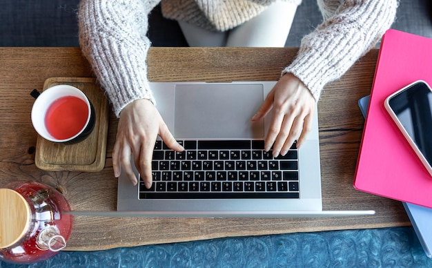 Mulher trabalhando em um laptop em um café com uma xícara de chá vista superior