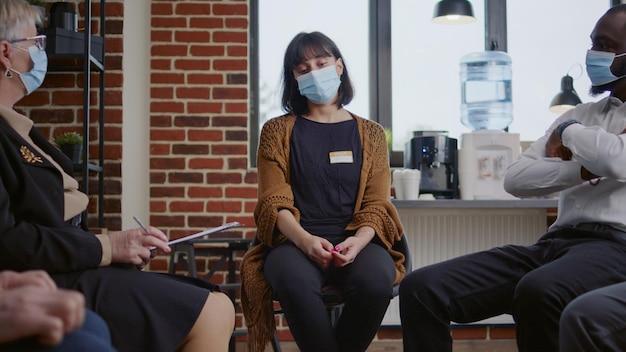 Mulher triste chorando em uma reunião de terapia na frente de um grupo de pessoas durante a pandemia de covid 19. Pessoa desesperada pedindo ajuda de psiquiatra no programa comunitário de reabilitação.