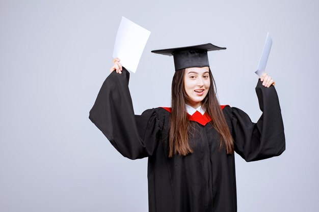 Mulher usando chapéu de formatura e roupão de cerimônia segurando papéis vazios. Foto de alta qualidade