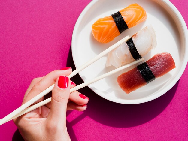 Mulher usando costeletas para escolher um sushi do prato