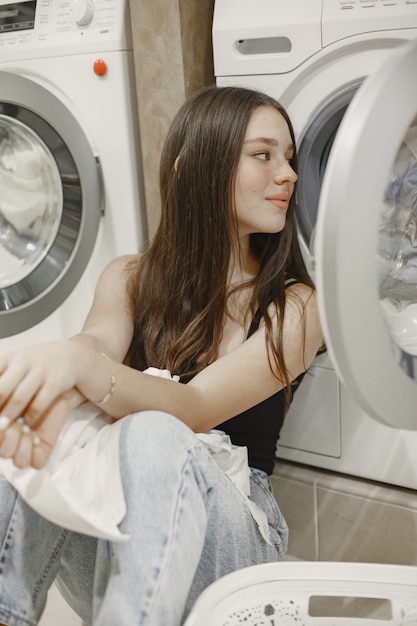 Mulher usando máquina de lavar, lavando a roupa. Jovem pronta para lavar roupas. Interior, conceito de processo de lavagem