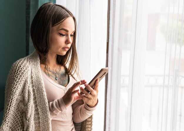 Mulher usando smartphone ao lado da janela em casa durante a pandemia