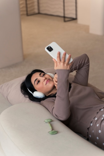 Mulher usando smartphone e fones de ouvido durante sua rotina de beleza