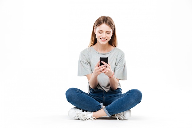 Mulher usando smartphone e sentada no chão