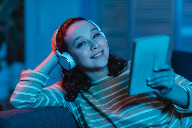 Mulher usando tablet e fones de ouvido em casa no sofá