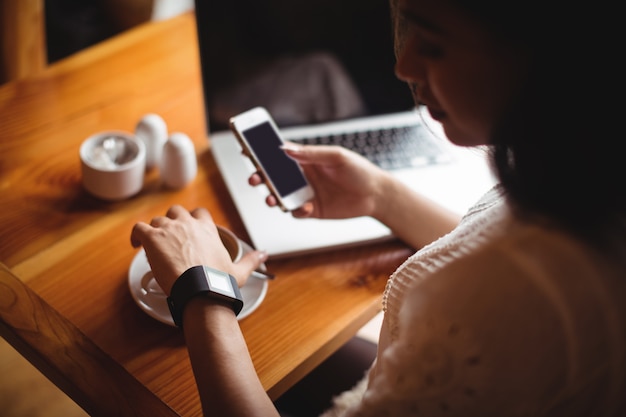 Mulher usando telefone celular enquanto toma uma xícara de café