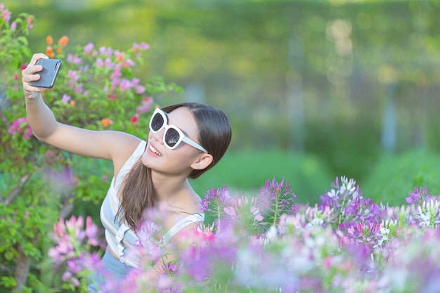 Mulher usando telefone celular para tirar foto no jardim de flores.