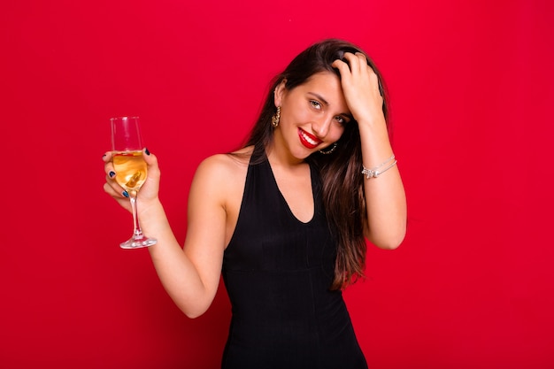 Mulher usando um vestido preto e segurando uma taça de champanhe posando em vermelho