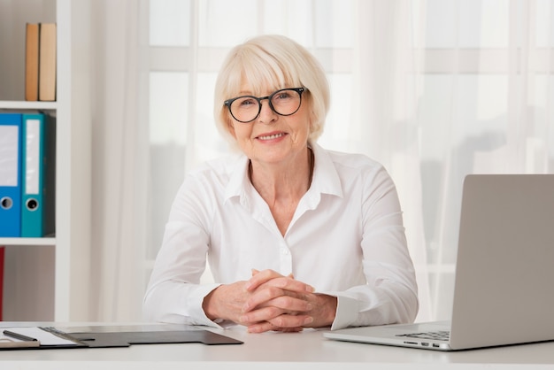 Mulher velha sorridente com óculos, sentado em seu escritório