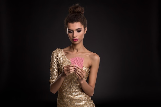 Mulher vencedora - jovem mulher em um elegante vestido de ouro segurando duas cartas, um pôquer de combinação de cartas de ases. Estúdio filmado em fundo preto. Emoções