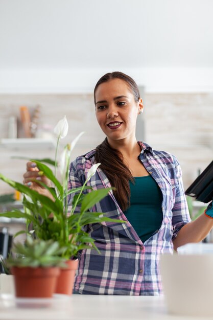 Mulher verificando flores na cozinha de casa e usando o tablet pc