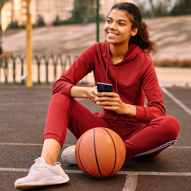 Mulher verificando o telefone ao lado de uma bola de basquete