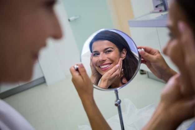 Mulher verificando sua pele no espelho depois de receber tratamento cosmético