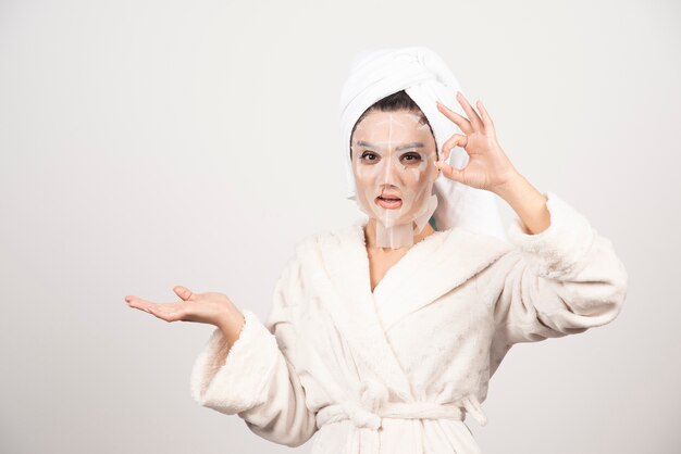Mulher vestindo roupão de banho e toalha com máscara.