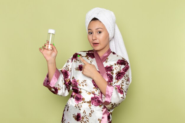 Mulher vestindo um roupão de banho com design de flor roxa segurando um frasco de spray de maquiagem