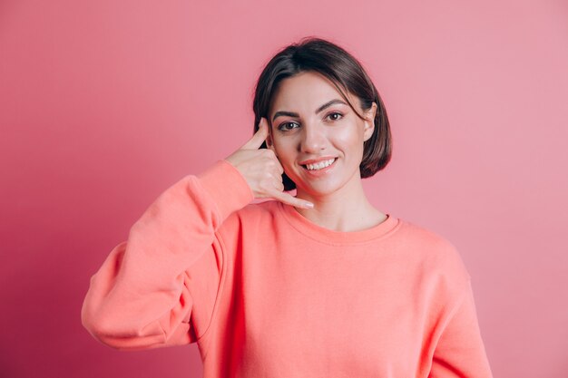 Mulher vestindo uma blusa casual no fundo sorrindo fazendo gesto de telefone com a mão e os dedos como se estivesse falando ao telefone