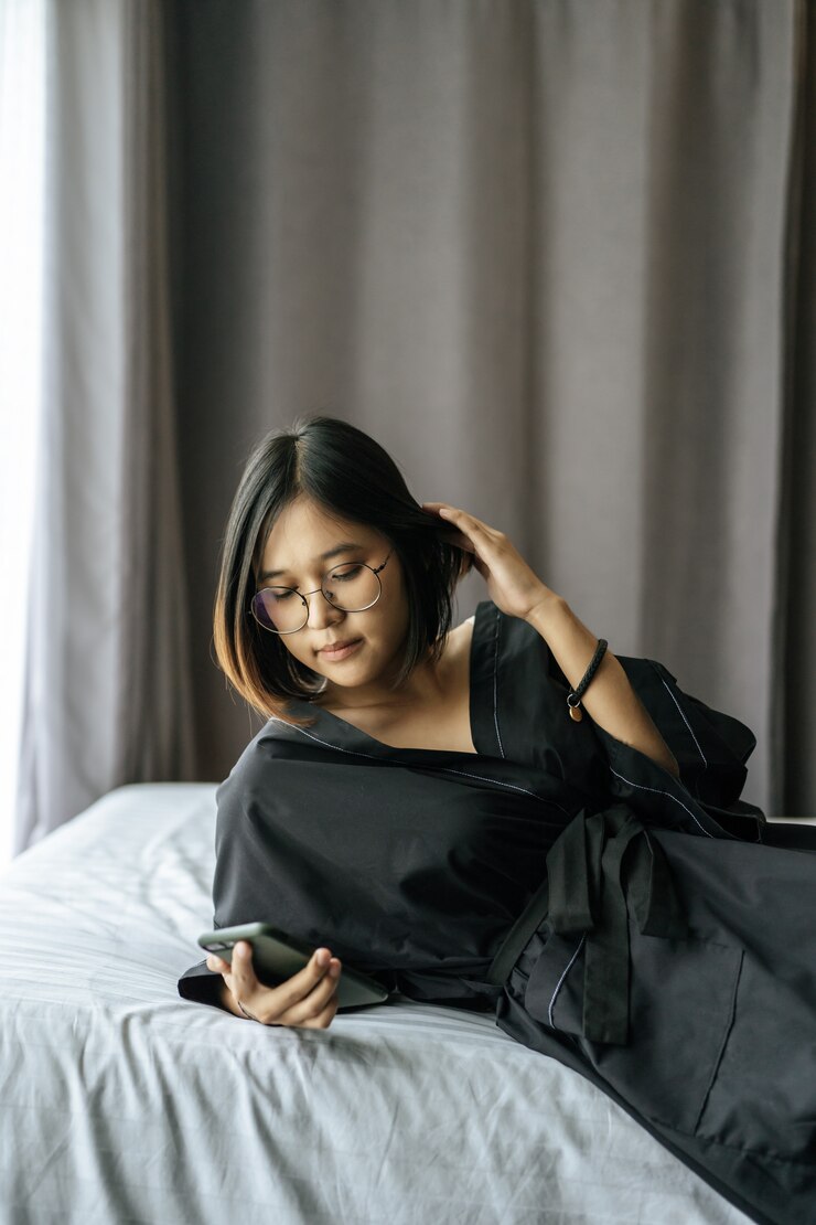 Foto grátis mulher vestindo uma camisa preta, deitada na cama e jogando smartphone.