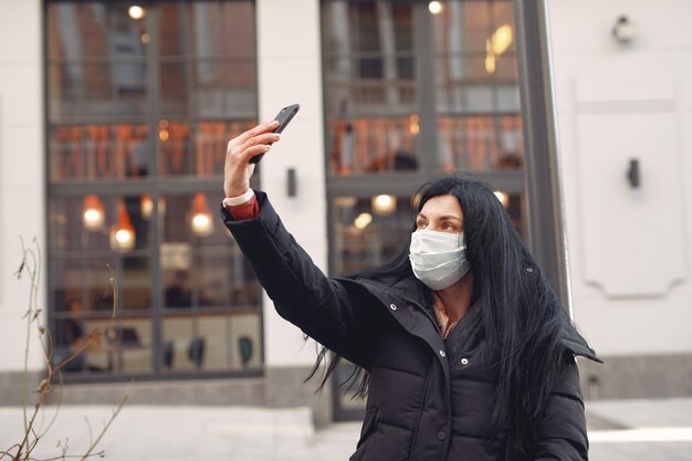 Mulher vestindo uma máscara protetora, sentado na rua, tomando uma selfie