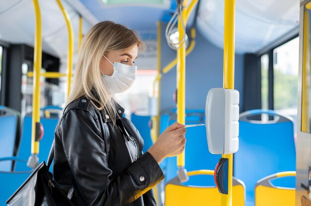 Mulher viajando de ônibus público usando máscara médica para proteção e usando passe de ônibus