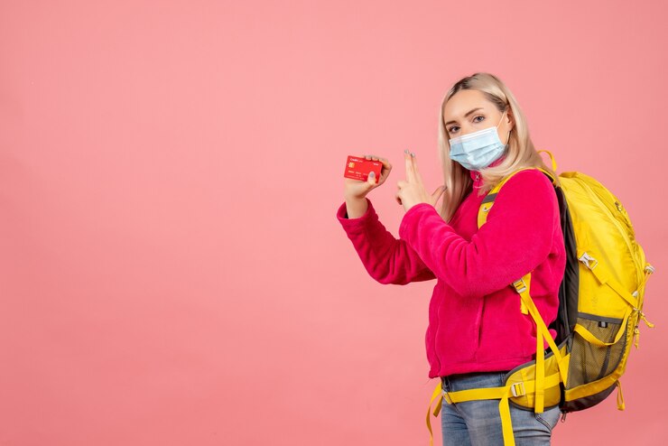 Foto grátis mulher viajante com mochila amarela usando máscara segurando cartão fazendo arma de dedo
