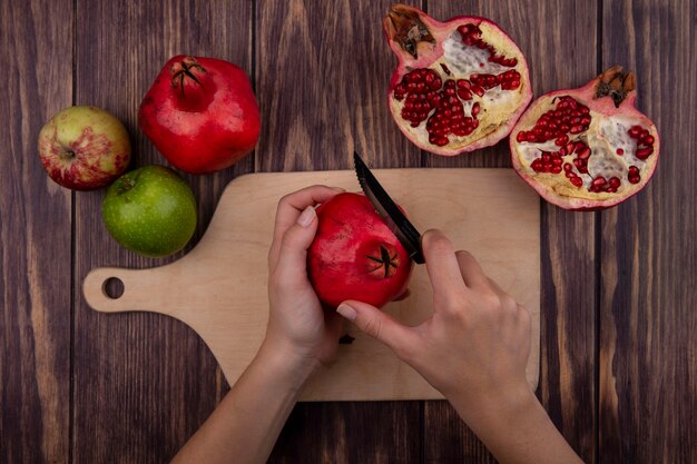 Mulher vista de cima cortando romã em uma tábua com maçãs na parede de madeira