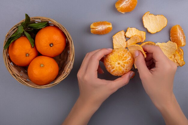 Mulher vista de cima descascando laranja com uma cesta em fundo cinza