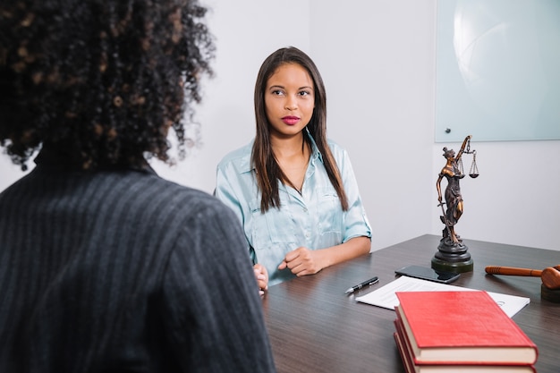 Mulheres afro-americanas, sentado à mesa perto de documento, caneta, figura e martelo