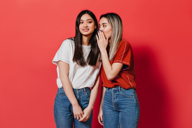 Mulheres asiáticas em camisetas largas fofocando na parede vermelha