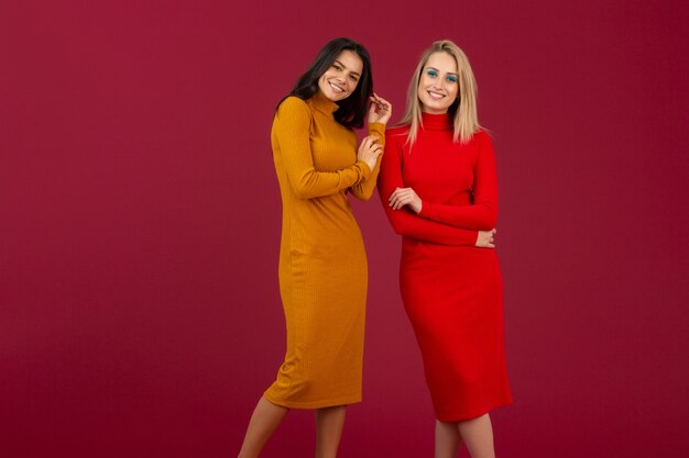 Mulheres bonitas e elegantes amigas em amarelo e vermelho outono inverno moda vestido de malha posando isolado na parede vermelha